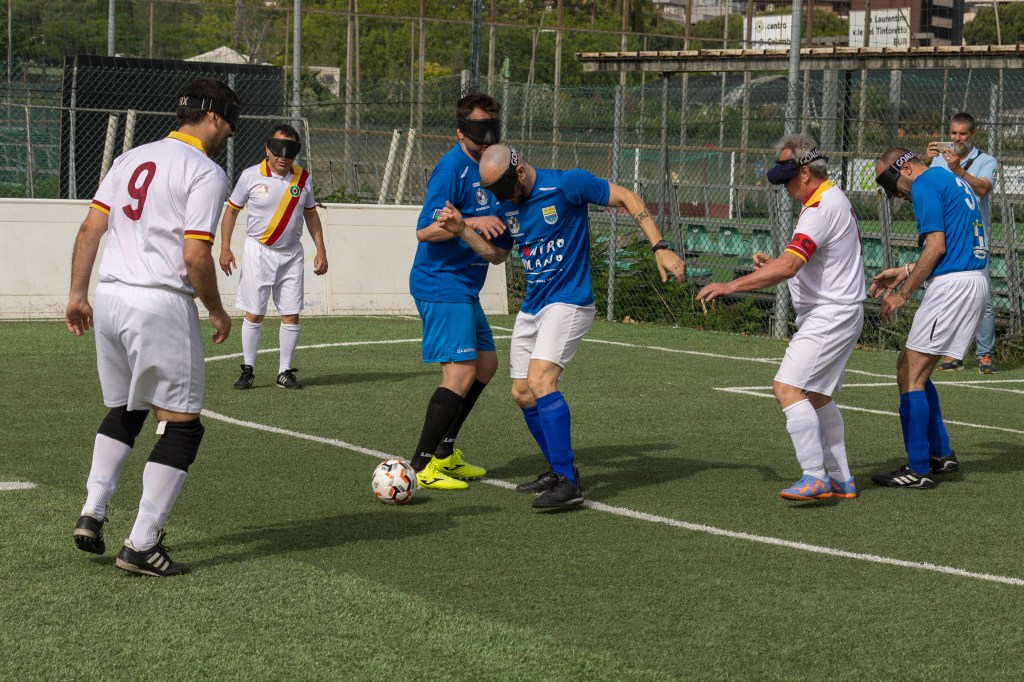 Evento Amichevole Nazionale Poeti. In foto un calciatore della squadra avversaria tenta di riprendere il pallone, circondato dai giocatori della Roma Blind Football. I calciatori della squadra avversaria indossano un completo azzurro. 
